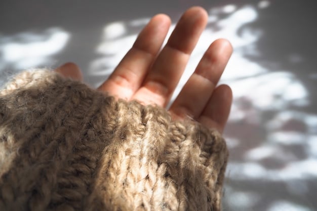 A hand touching a thick knitted winter sweater, focusing on the texture and the quality of the yarn.