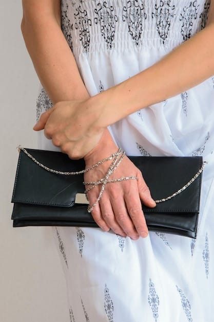 Close-up of a woman's hands clasping a sparkly clutch purse. She's wearing several delicate gold bracelets and rings. The focus is on the jewelry and accessories that elevate a simple outfit.