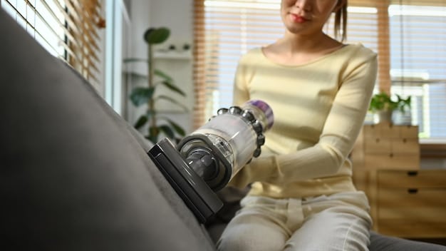 A close-up shot of a person vacuuming a SHEIN fabric armchair with a handheld vacuum cleaner. The focus is on the nozzle and the fabric fibers.