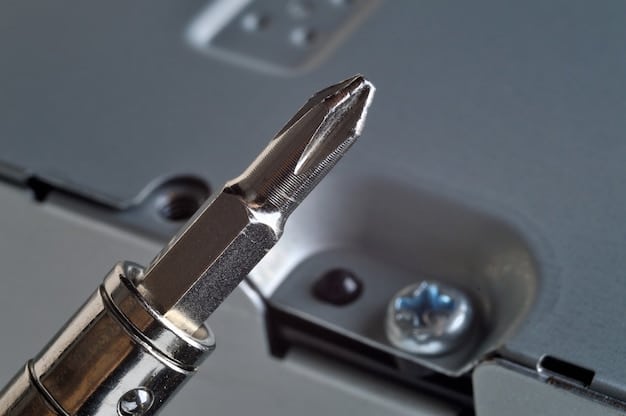 Close-up shot of a hand using a screwdriver to replace a laptop battery. The focus is on the battery compartment and the new battery being installed. The background is blurred, but tools and components indicate a DIY repair setting.